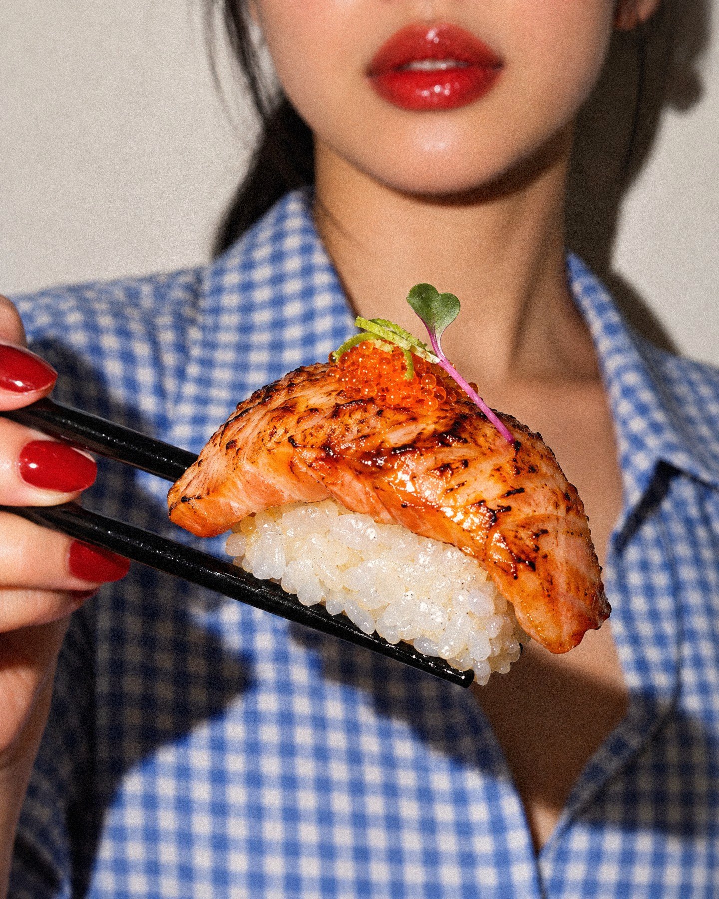 A guest holding a torched salmon nigiri up to the camera