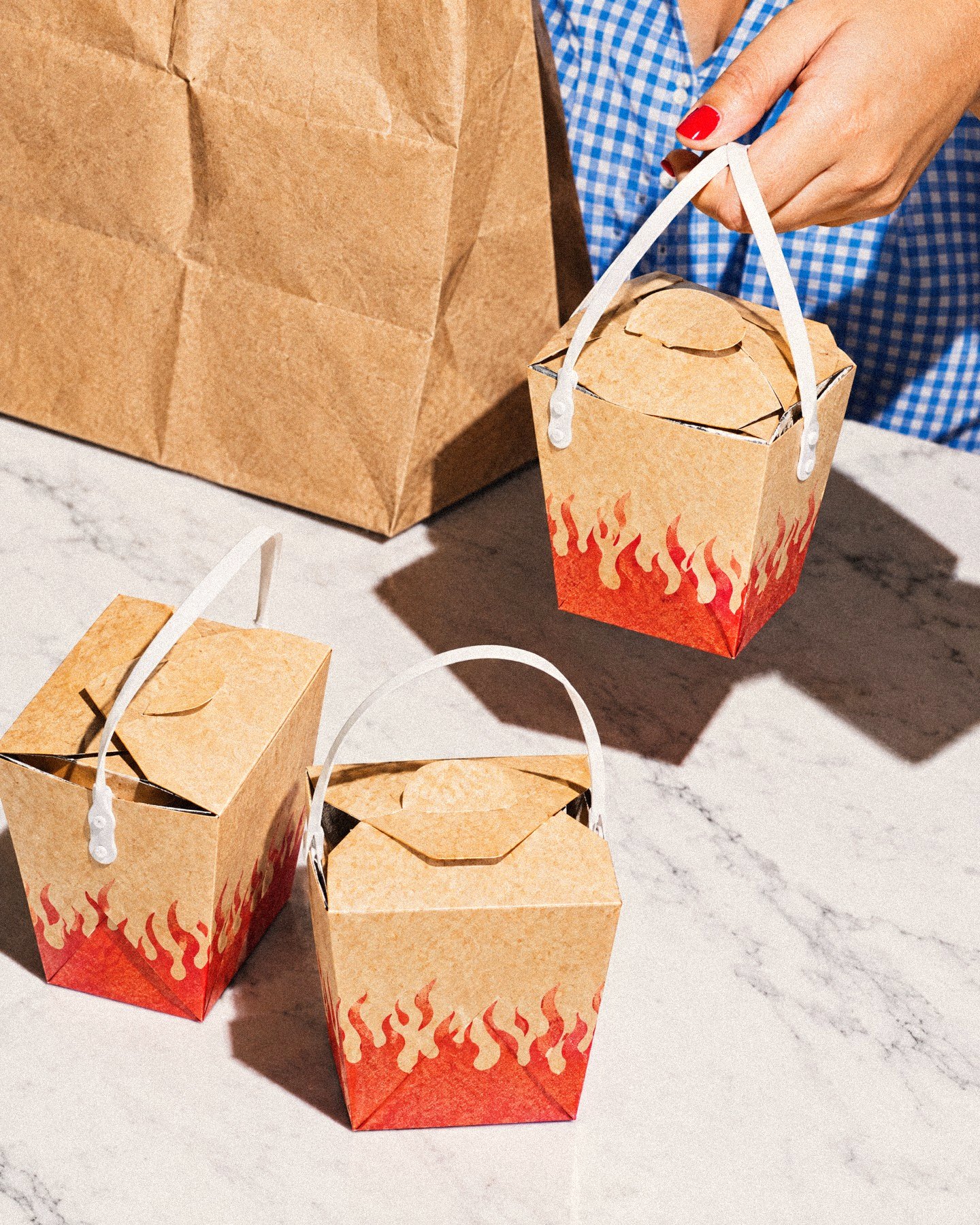 Hands packing flame-print carryout pails into a kraft bag